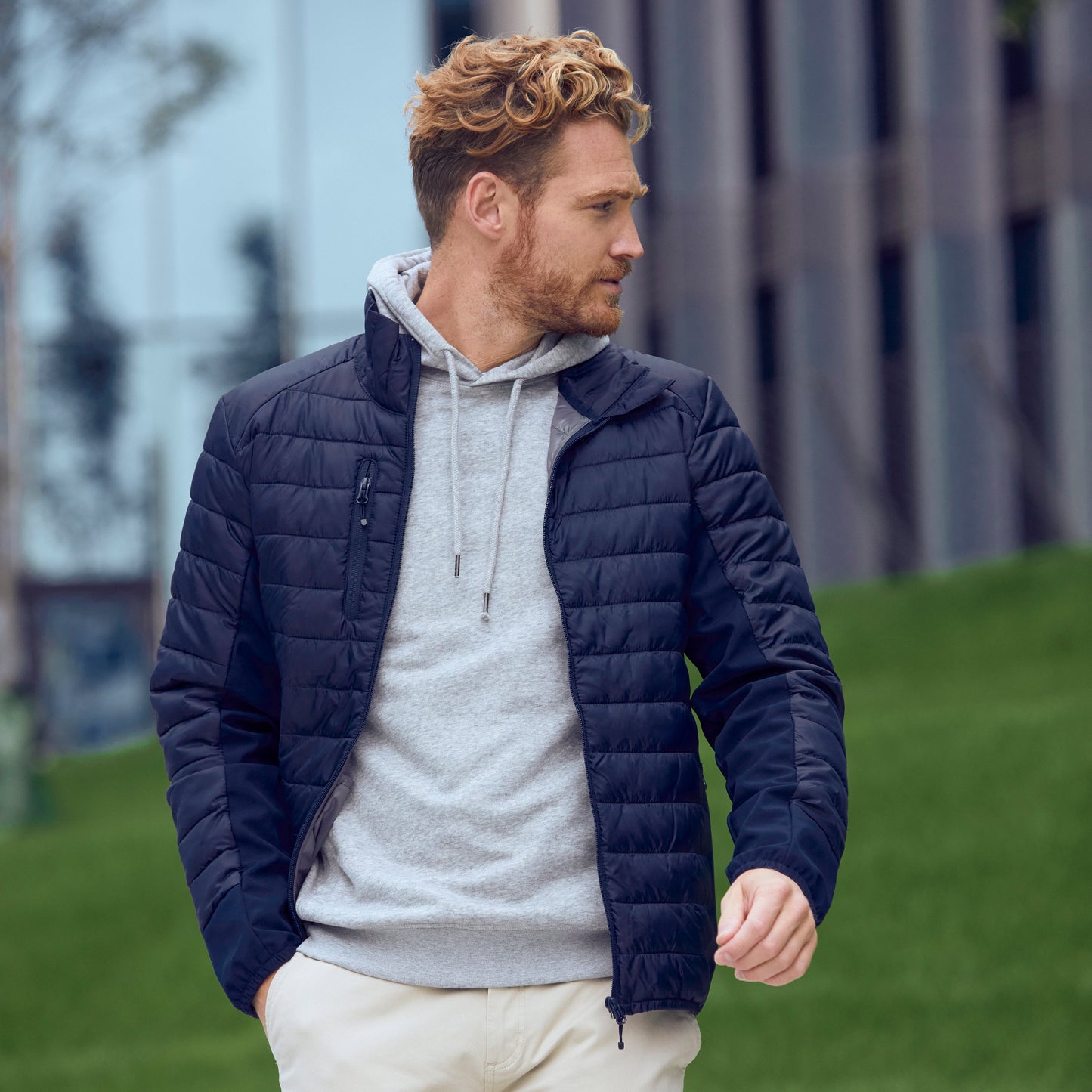 Man wearing a navy puffer jacket over a gray hoodie with white pants outdoors.