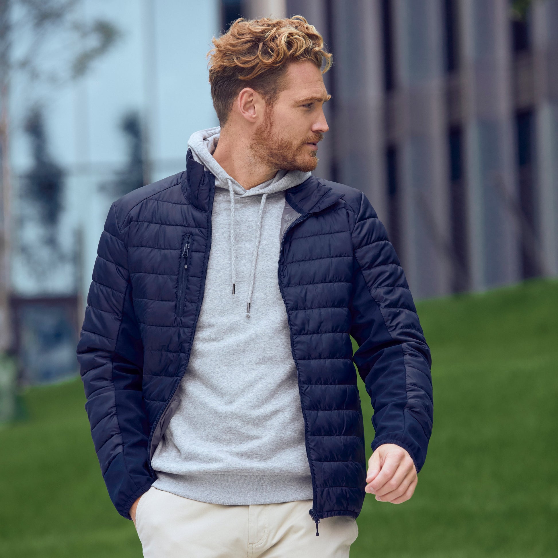 Man wearing a navy puffer jacket over a gray hoodie with white pants outdoors.