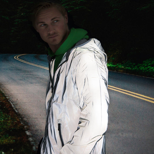 Person standing on a dark road with a green jacket and white coat.