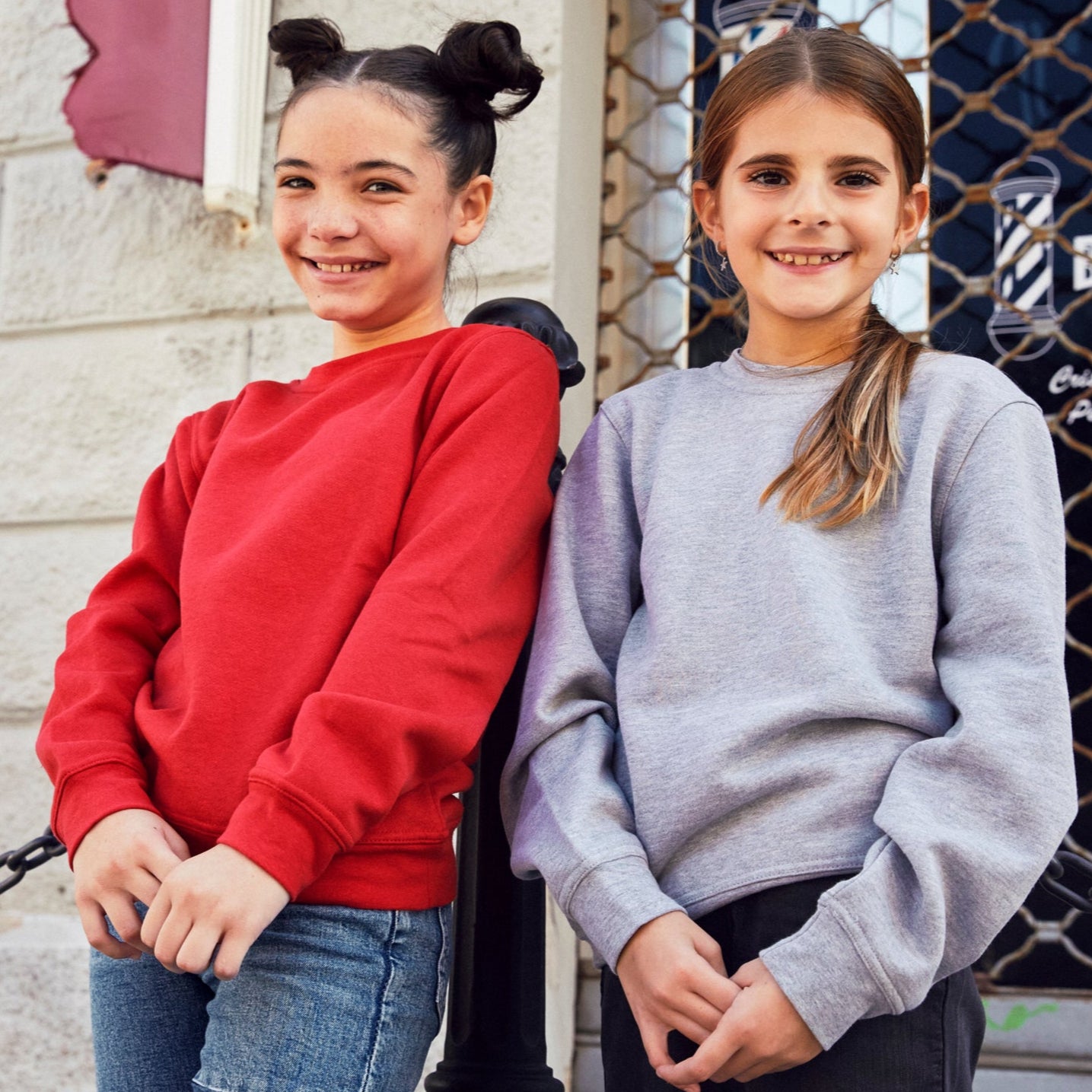 Two young girls standing outside a building with a sign that reads 'Barber Shop'.