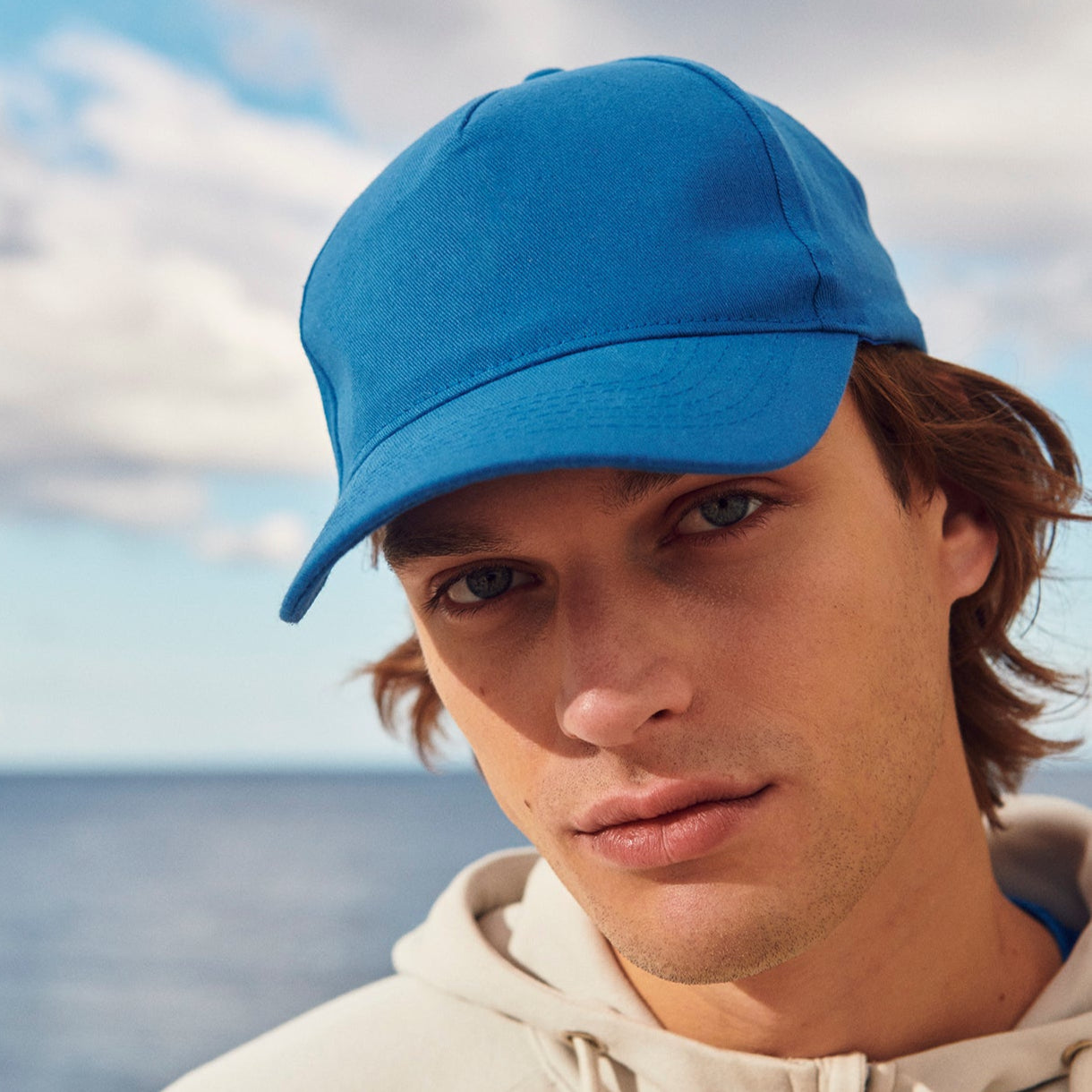Man wearing a blue cap and beige hoodie by the ocean