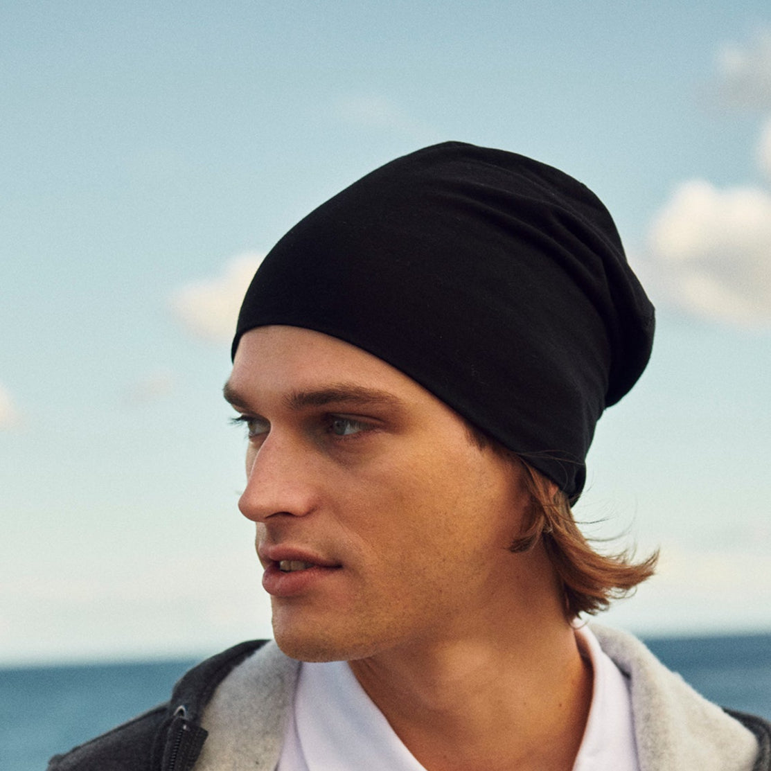 Man wearing a black beanie and white shirt with a blurred ocean background
