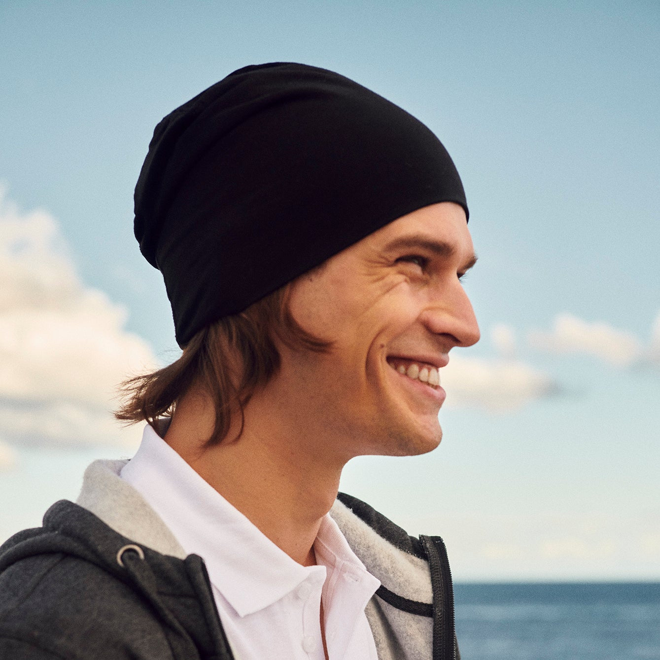 Man wearing a black beanie and dark jacket by the ocean