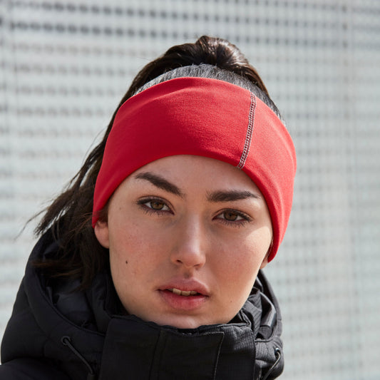 Woman wearing a red headband and black jacket against a textured wall.
