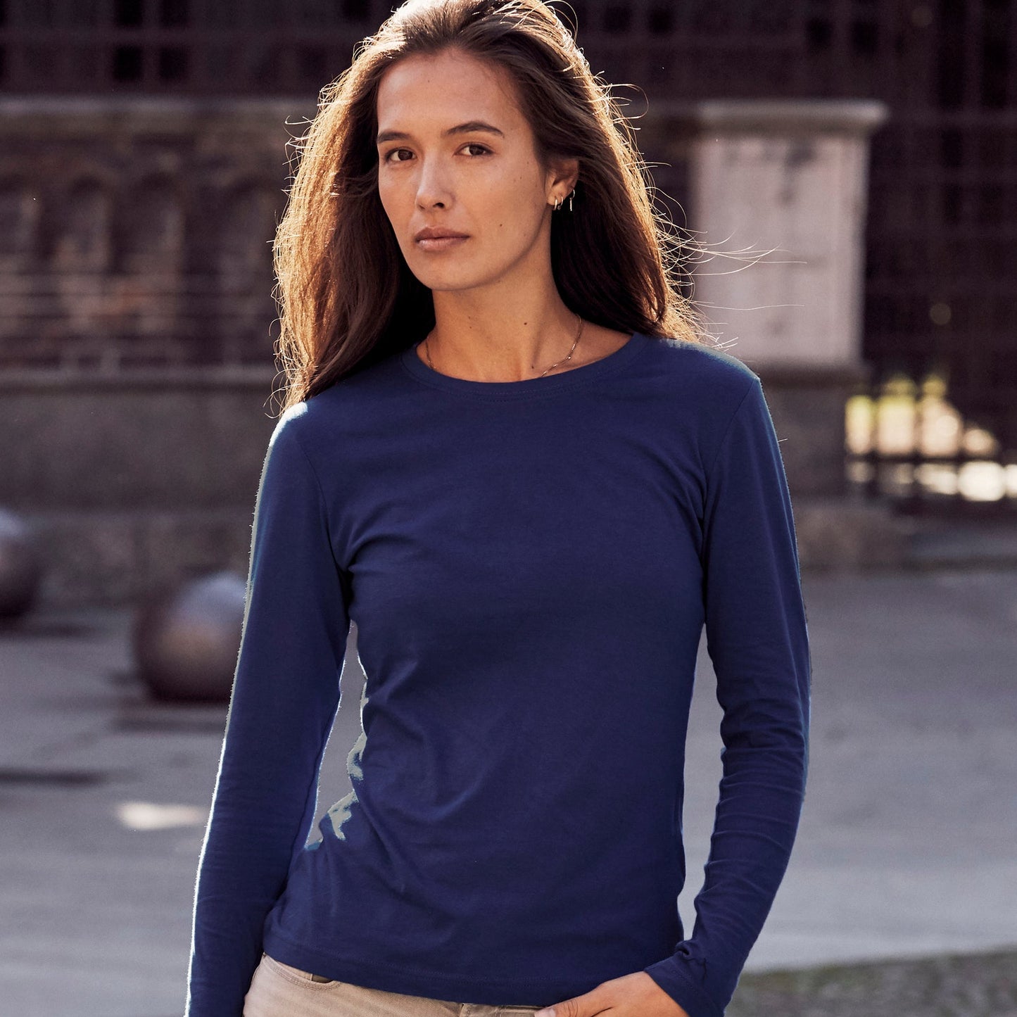 Woman wearing a blue long-sleeve top and beige pants standing on a stone path.