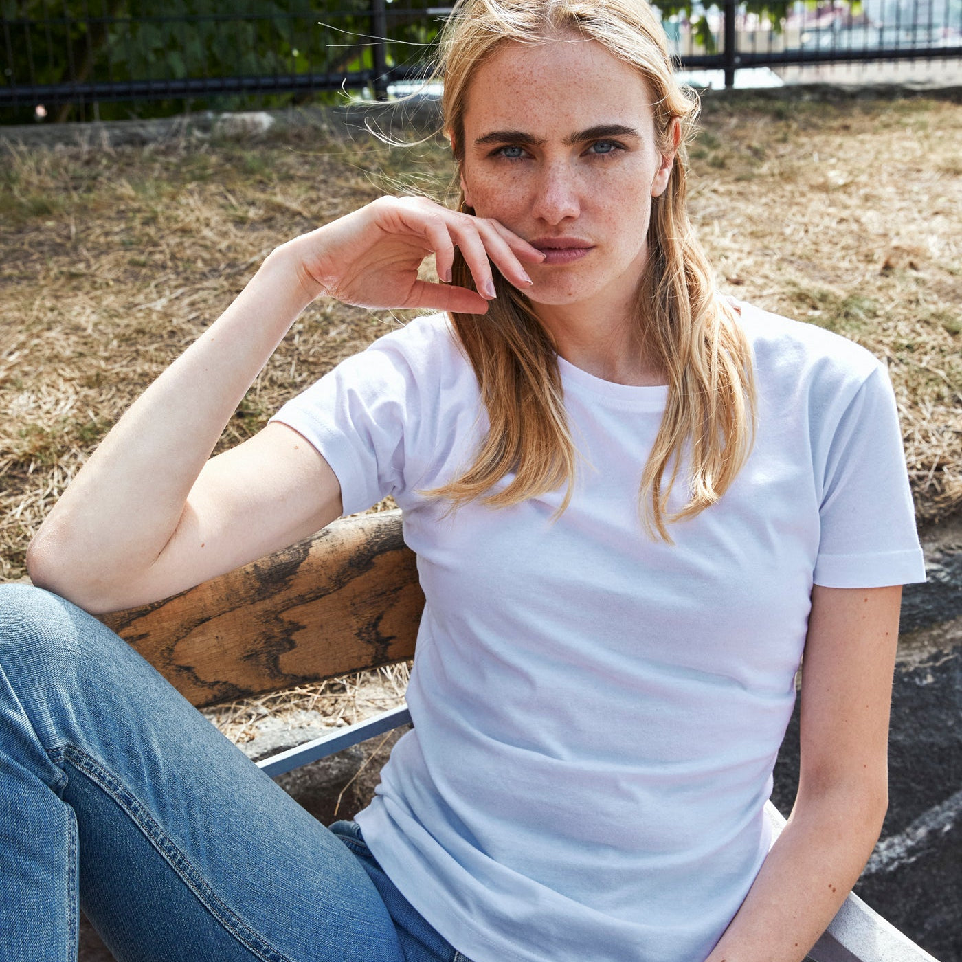 Woman sitting outdoors holding a coffee cup, wearing a white t-shirt and blue jeans.