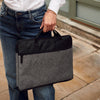 Woman in a white shirt and jeans holding a phone and a black bag on a sidewalk.