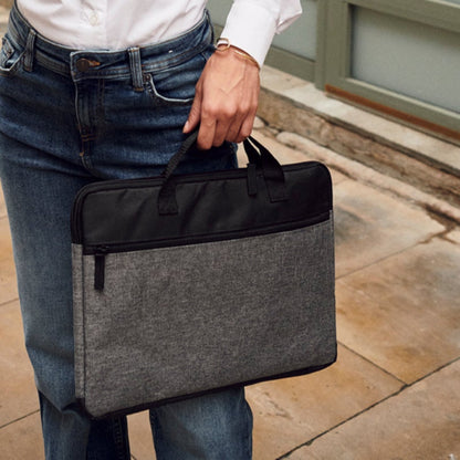 Woman in a white shirt and jeans holding a phone and a black bag on a sidewalk.