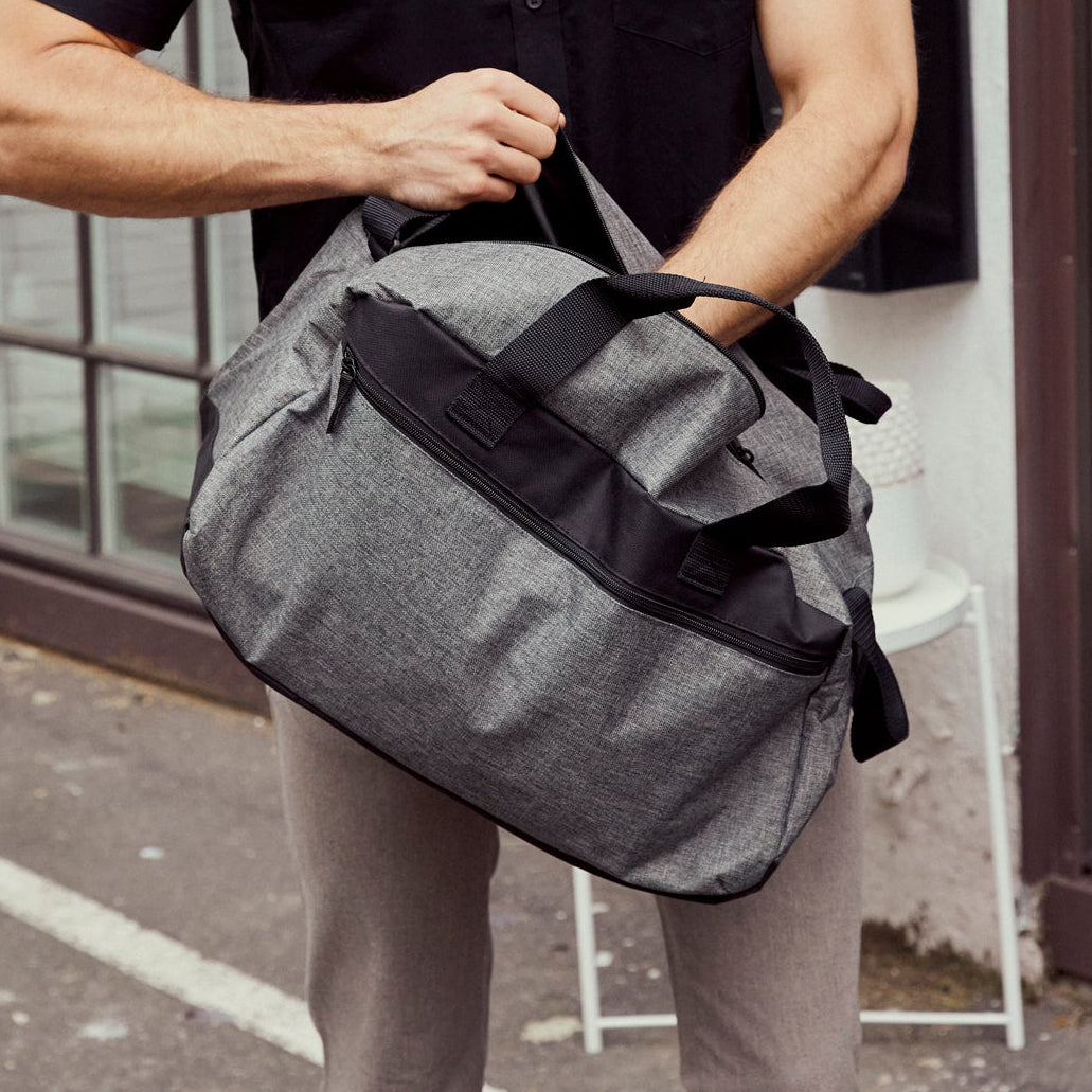 Man holding a gray duffel bag in an urban setting