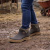 Person wearing brown boots with a rustic outdoor setting featuring cows and a barn.