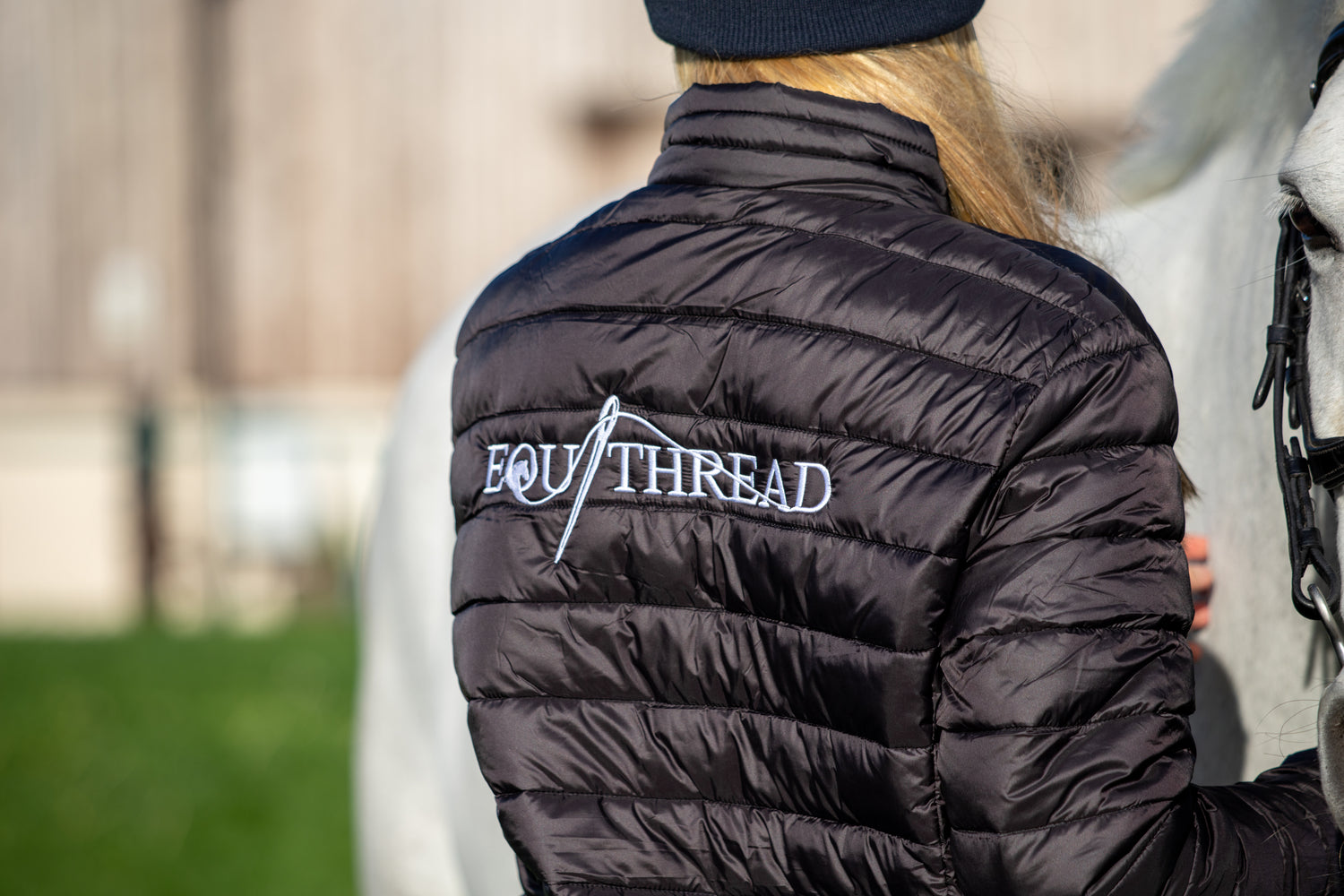 Person wearing a black puffer jacket with 'Equithread' logo, standing next to a horse.